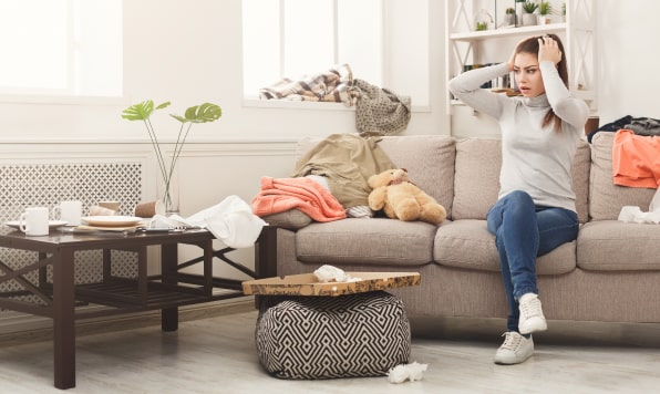 Desperate woman sitting on the sofa in a cluttered living room.